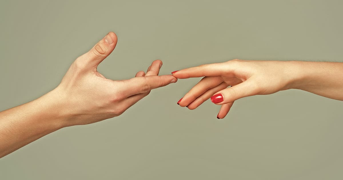A man's hand and a woman's hand reaching toward each other, fingertips almost touching, on a gray-green background.